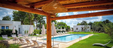 A pool area with lounge chairs and umbrellas, a covered seating area, and a view of the surrounding landscape.