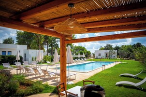 A pool area with lounge chairs and umbrellas, a covered seating area, and a view of the surrounding landscape.