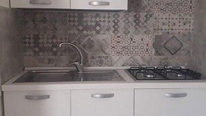 A kitchen with a sink, stove, and patterned backsplash. - Masseria Scianne (Nardò)
