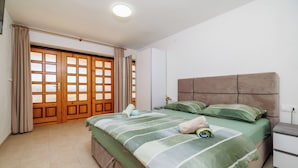 A bedroom with a large bed, a nightstand, a wardrobe, and a sliding glass door.
