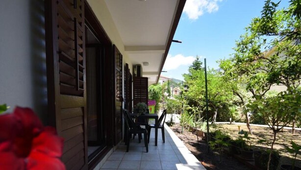A covered outdoor area with a table and chairs, surrounded by greenery and a view of a building in the background. - Cozy Igalo Retreat Ideal for Families (Igalo)