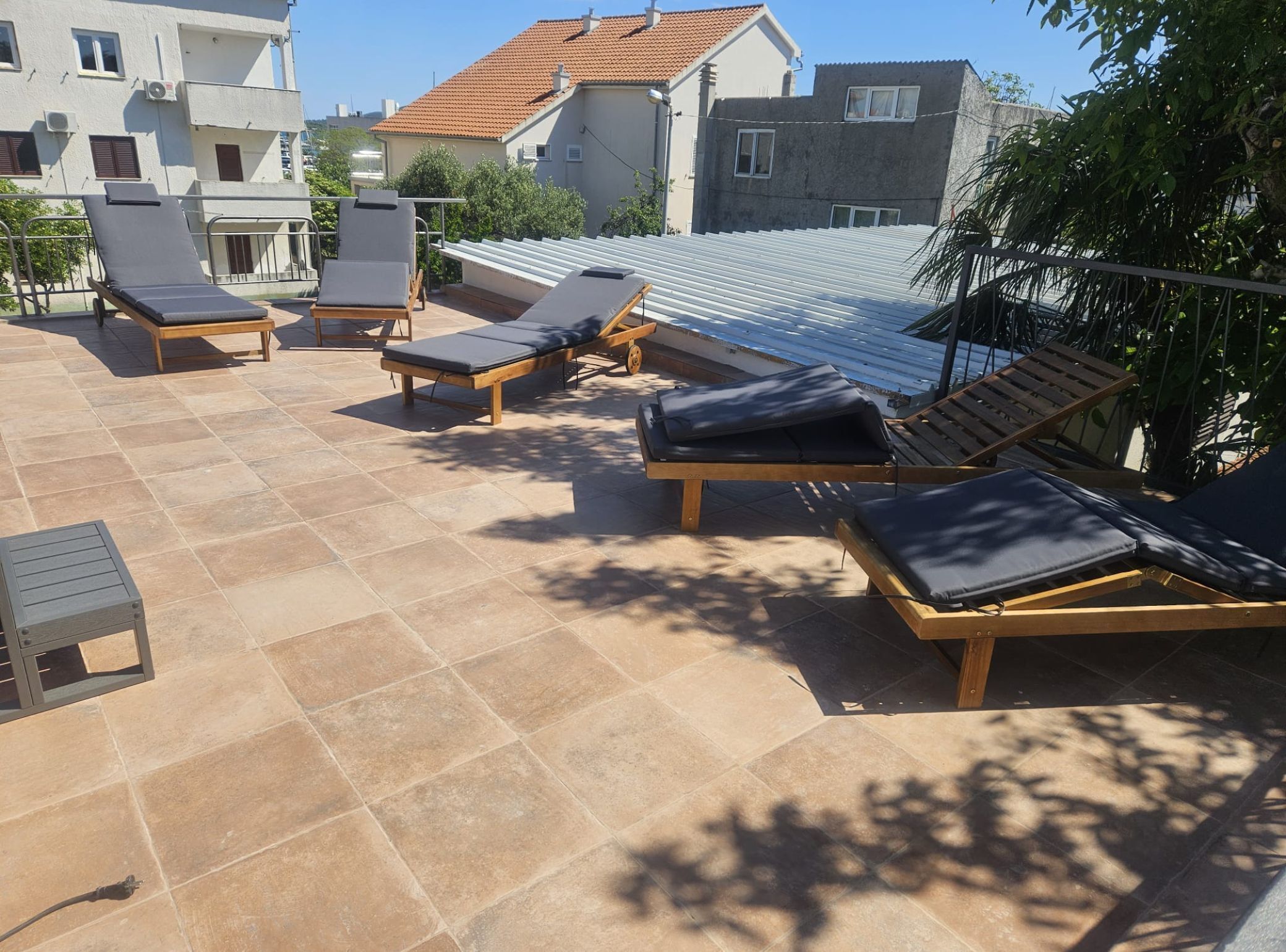 A rooftop terrace with multiple sun loungers and a small table, surrounded by buildings.