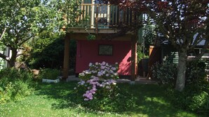 A two-story house with a balcony, surrounded by lush greenery and flowering plants. - Quiet retreat in rural Cornish garden. (Truro)