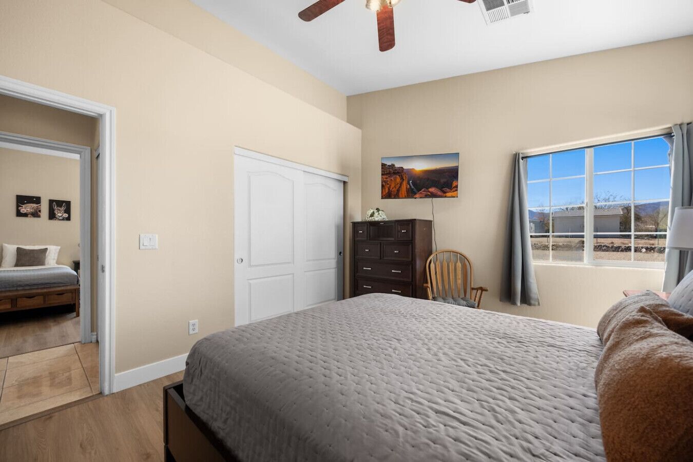 Un dormitorio con cama, cómoda, silla, ventana con vistas y ventilador de techo.
