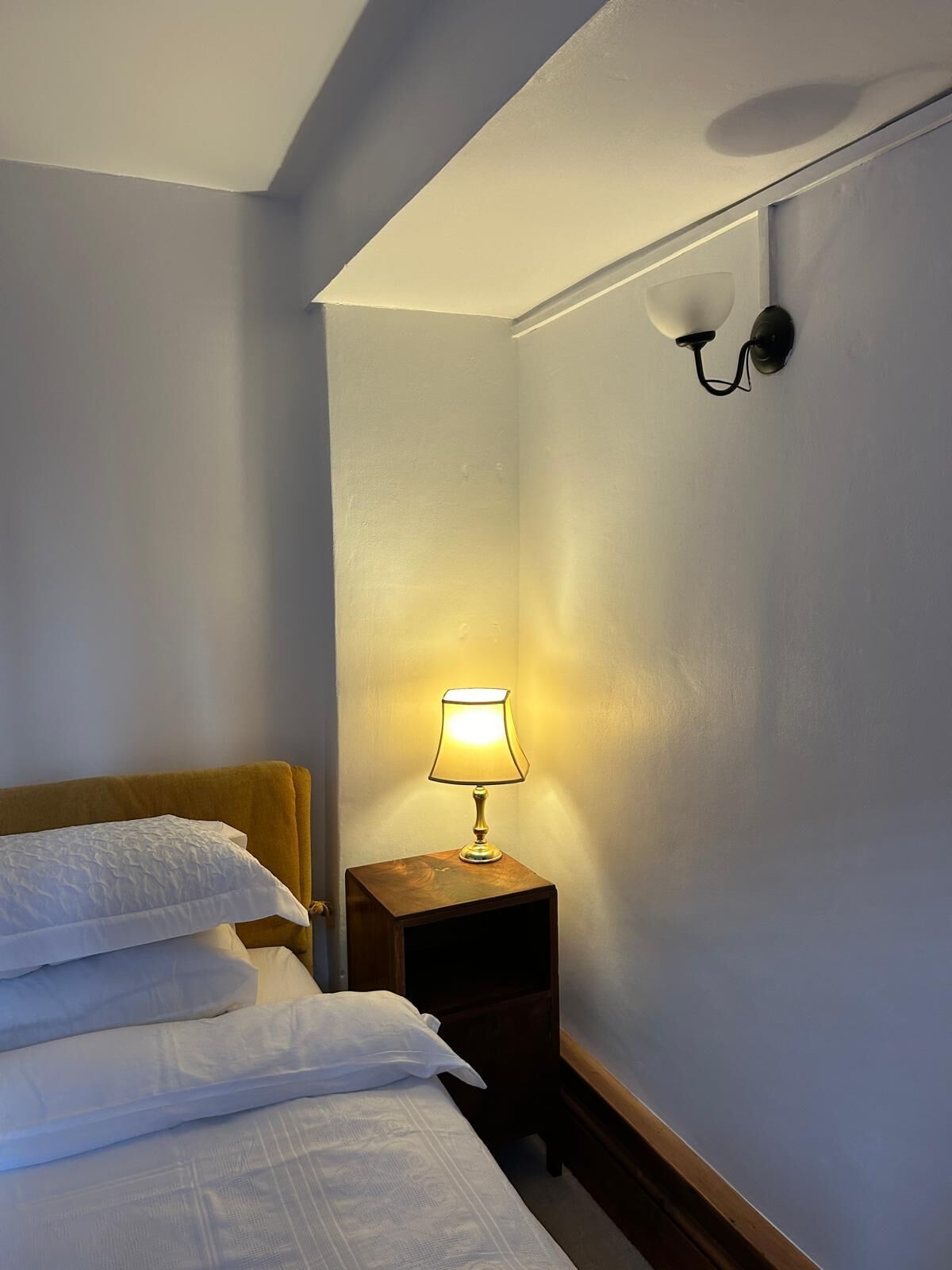 Habitación de hotel con una cama, una mesita de noche con lámpara y una lámpara de pared.