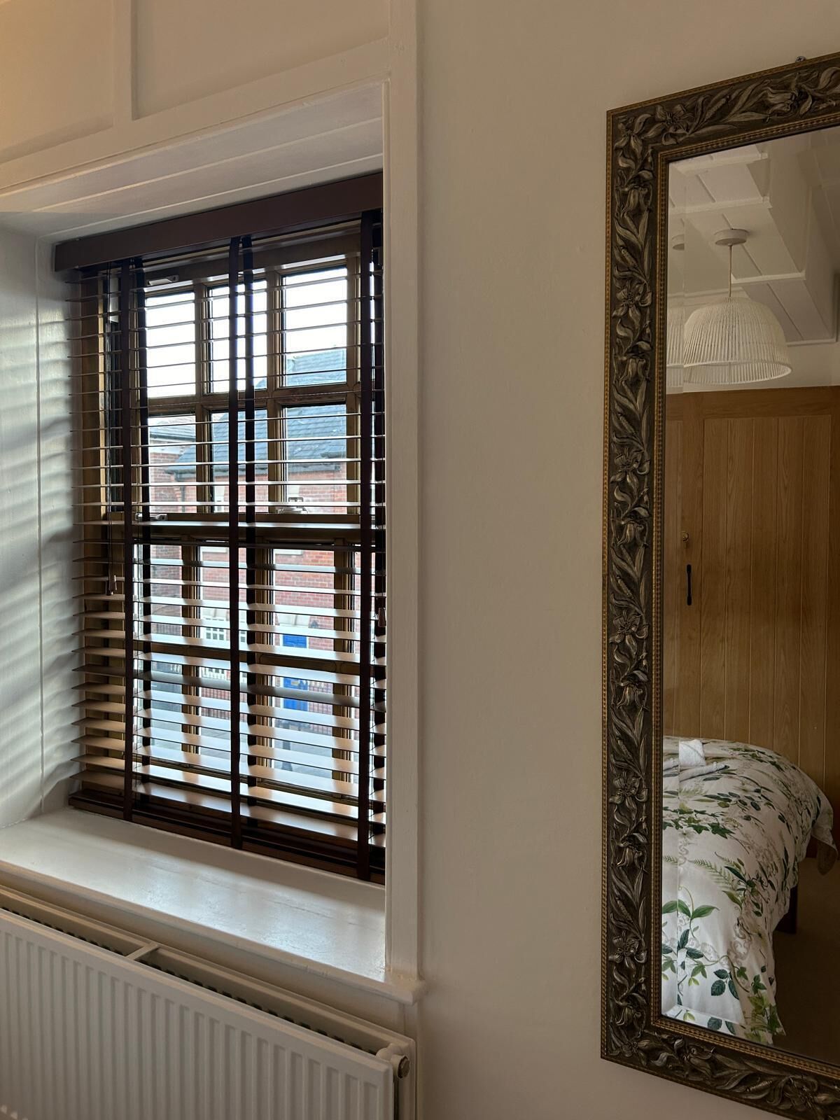 A room with a window with blinds, a radiator, and a large mirror on the wall.