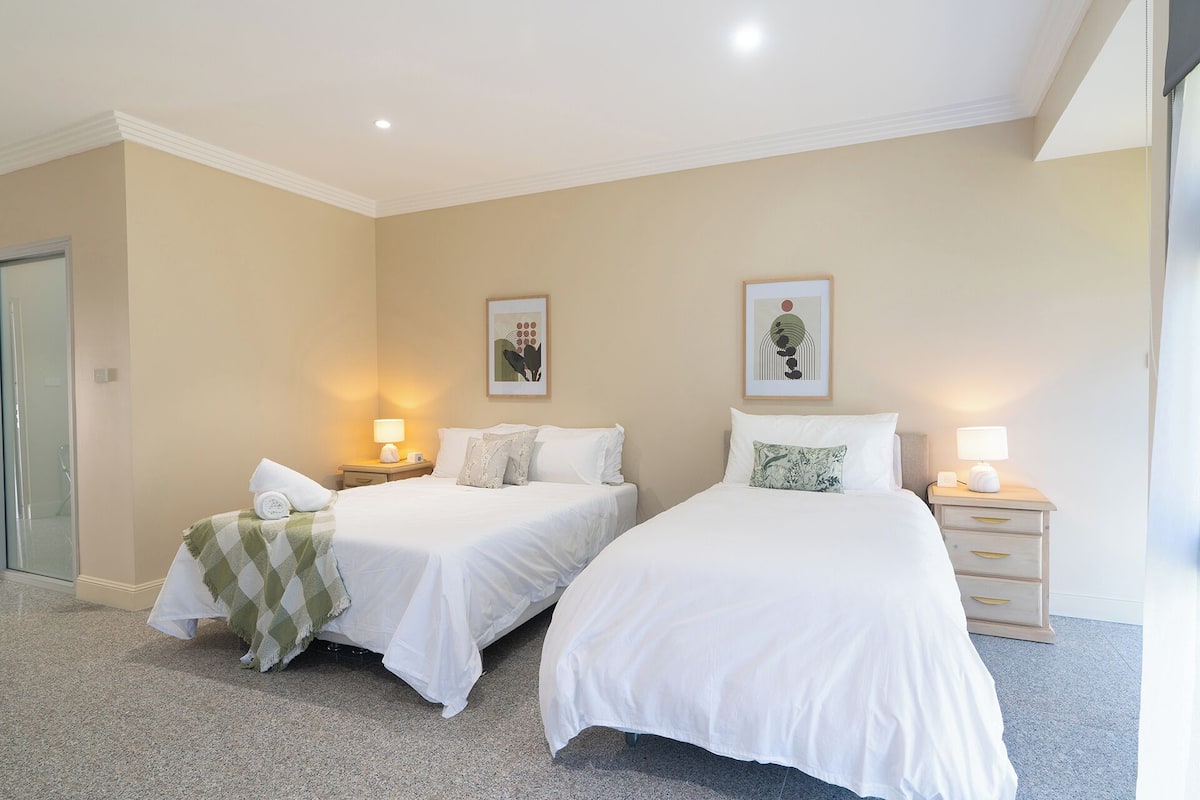 A hotel room with two single beds, each with a bedside table and lamp, and a large mirror on the left wall.