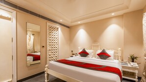 A hotel room with a large bed, a bedside table with a phone, and a mirror on the wall. - The Pinky Villa Heritage Boutique Suites (New Delhi)