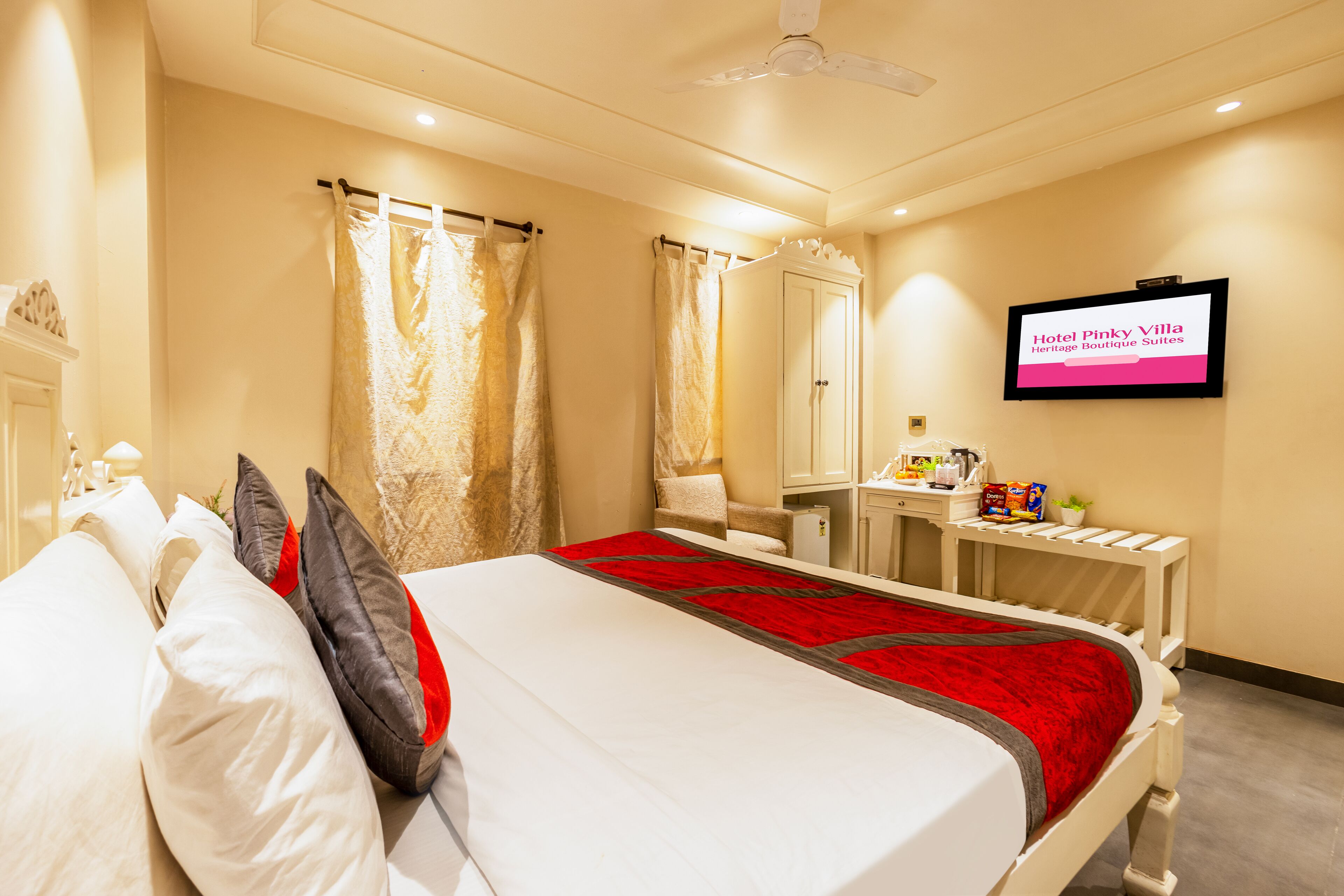 Quarto de hotel com cama, escrivaninha, cadeira, televisão e espelho.