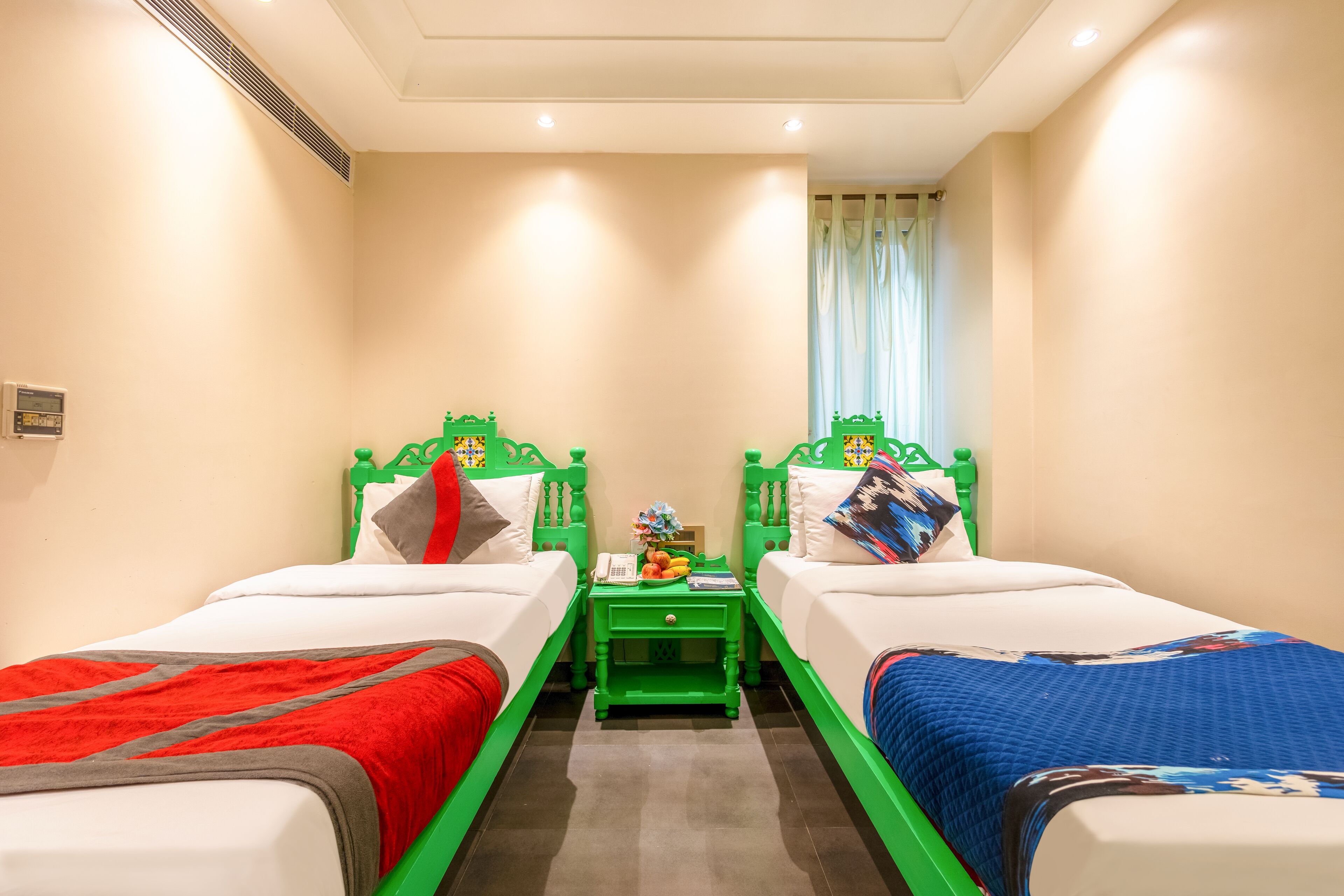 Une chambre d’hôtel avec deux lits simples, une table de chevet verte et une fenêtre avec des rideaux.