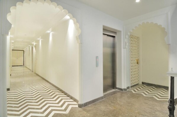 A hotel corridor with a patterned floor, an elevator, and decorative arches. - The Pinky Villa Heritage Boutique Suites (New Delhi)