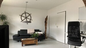 A modern living room with a black sofa, a wooden coffee table, and a black office chair. - Work & Relax - Your workation / vacation apartment on the North Sea with stable WLAN (Eddelak)