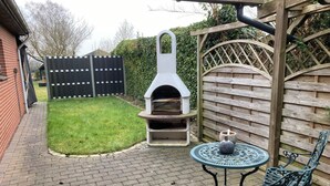 A patio area with a brick floor, a pizza oven, a table with chairs, and a wooden fence in the background. - Work & Relax - Your workation / vacation apartment on the North Sea with stable WLAN (Eddelak)