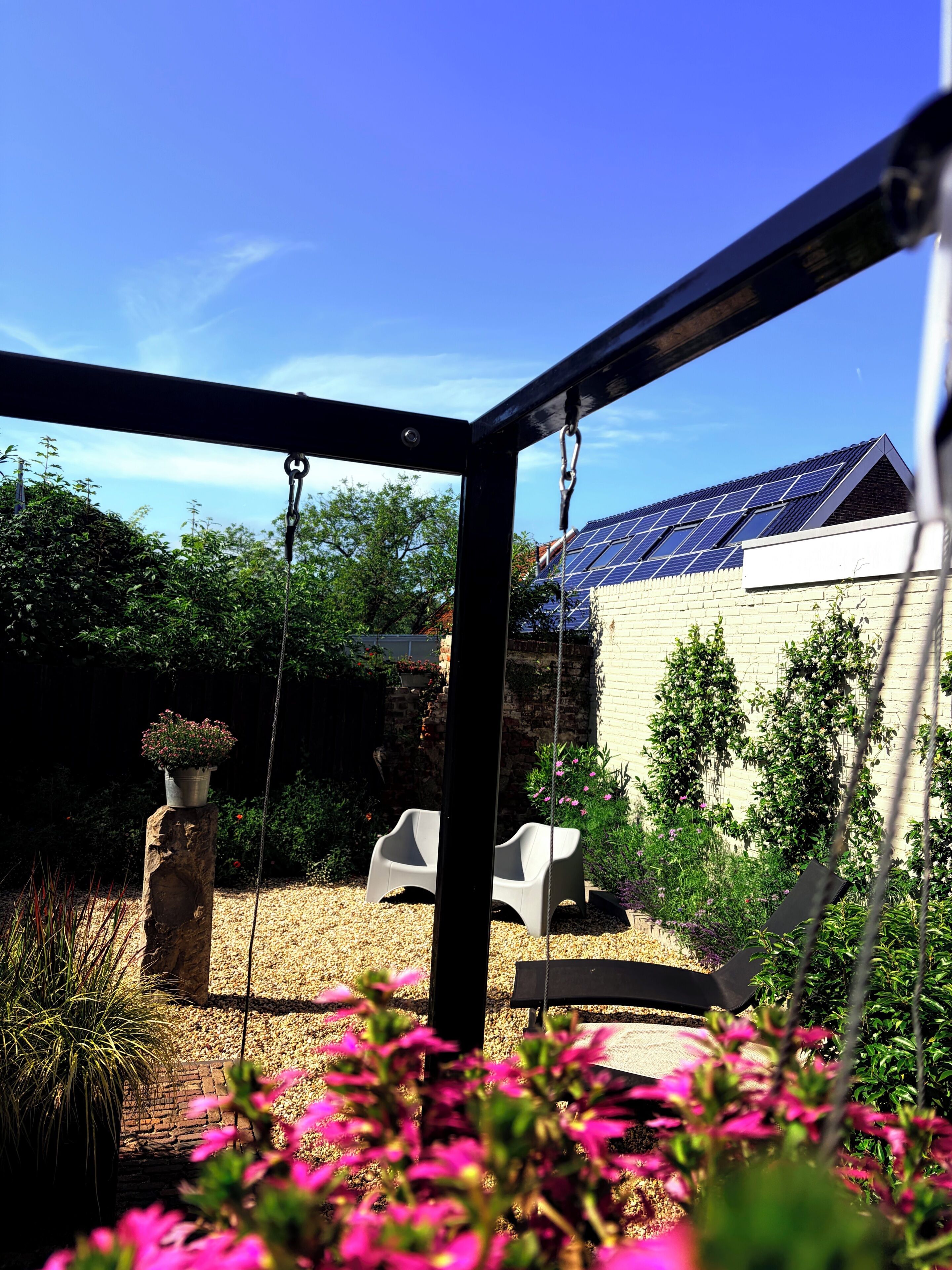 Een tuin met een schommel, een bakstenen muur en een gebouw met zonnepanelen.