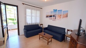 A living room with a sofa, a coffee table, a TV, and a window with curtains. - Wide House With Private Fenced Garden in Lignano Pineta (Lignano Sabbiadoro)