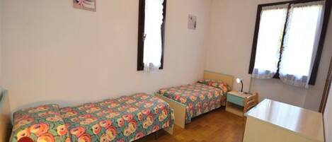 A room with two single beds, a small desk, and a chair.