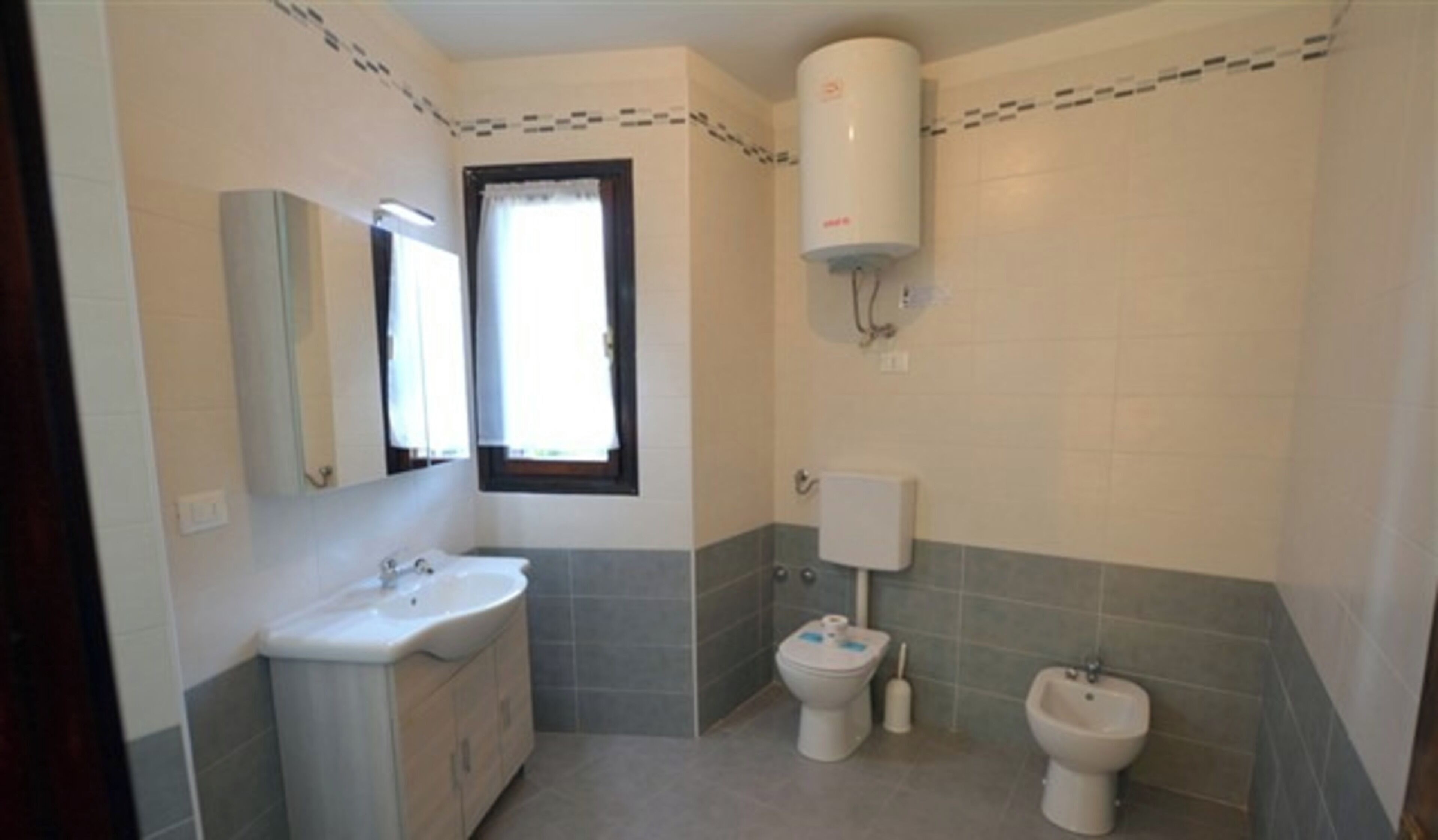 A bathroom with a sink, toilet, bidet, and a window with curtains.