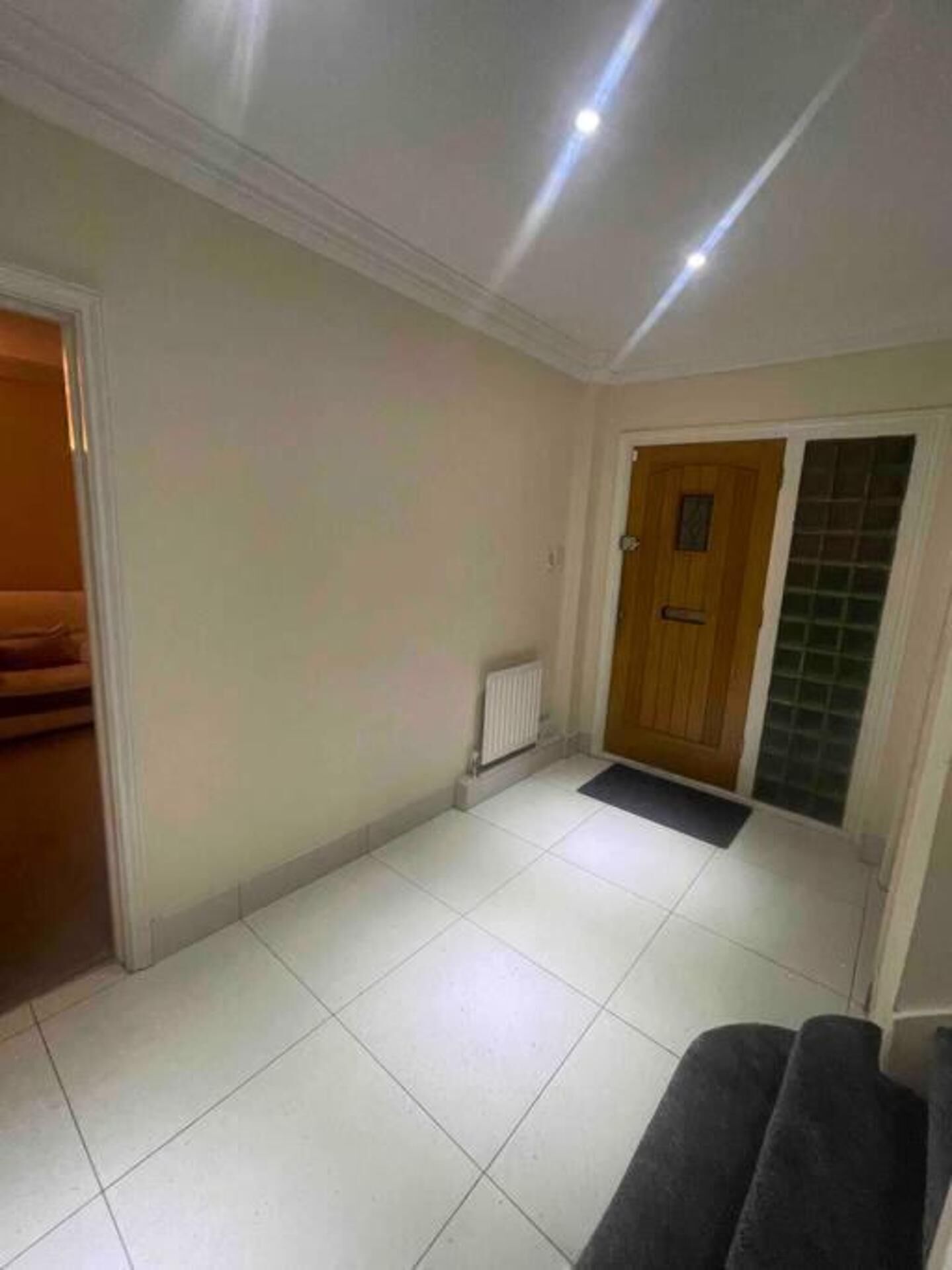 A hallway with white tiled floors, a wooden door, and a radiator.