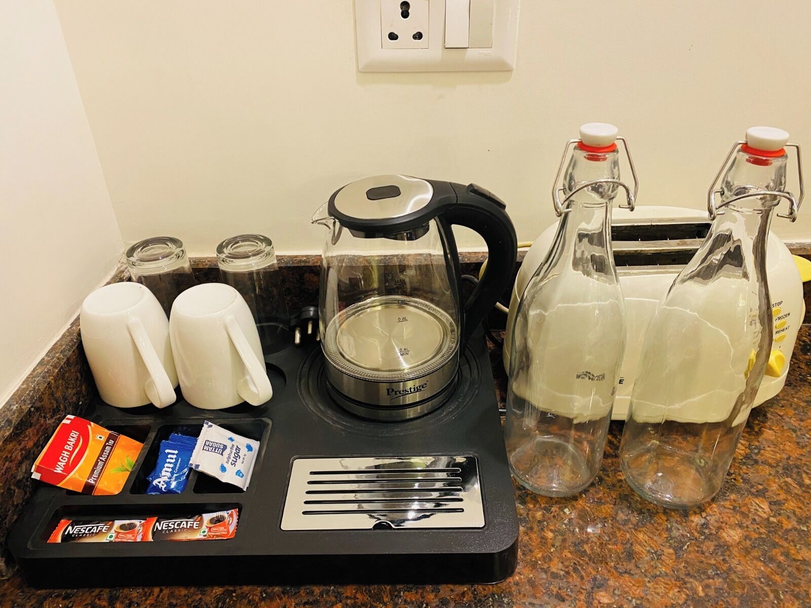 A coffee maker, two mugs, a glass carafe, a toaster, and a tray with coffee pods and sugar packets.