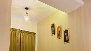 Een kamer met een bruine bank, twee gele fauteuils, een kleine tafel en drie ingelijste foto’s aan de muur.