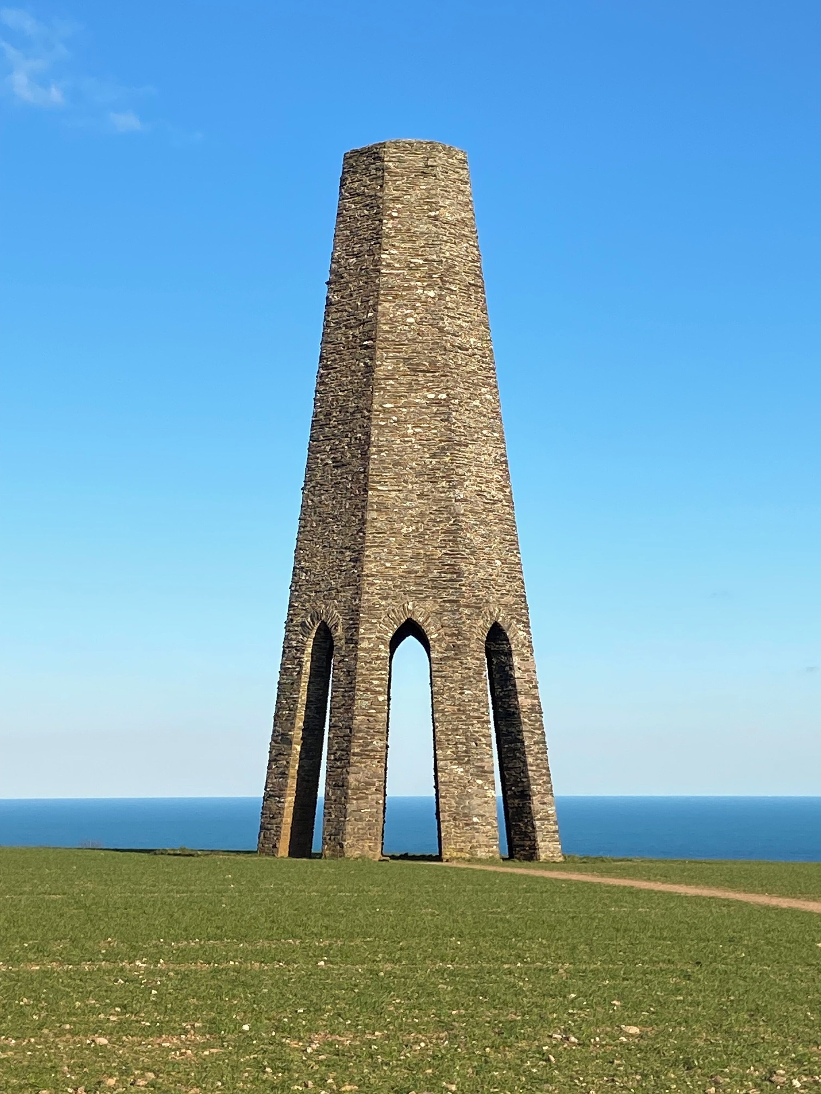 Une haute tour de pierre, dotée de trois arcades à sa base, se dressant sur un ciel bleu clair.