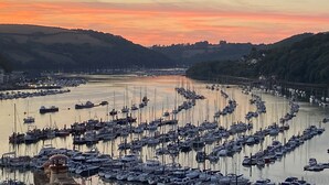 Un puerto deportivo con numerosas embarcaciones amarradas, rodeado de colinas y con un atardecer al fondo.
