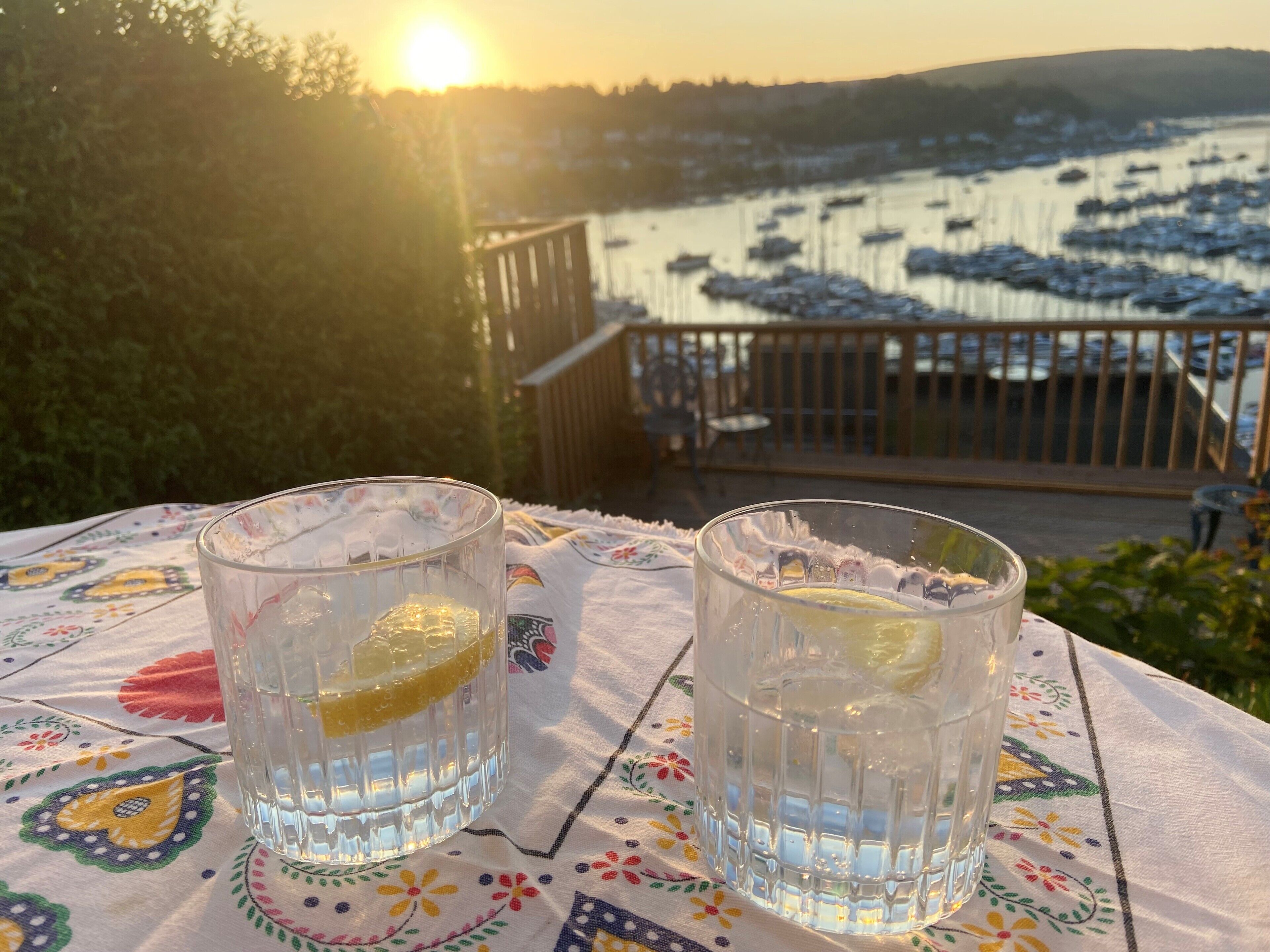 Dos vasos de agua con rodajas de limón sobre una mesa con mantel floreado, con vistas a un puerto deportivo con barcos.