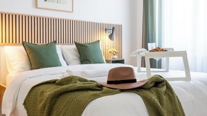 A neatly made bed with a green blanket and a brown hat, a wooden headboard, and a bedside table with a lamp.