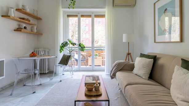 A modern living room with a beige sofa, a coffee table, and a dining area with a table and chairs.
