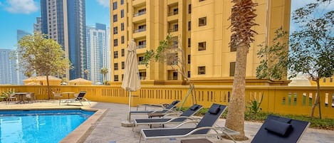 A poolside area with lounge chairs, a pool, and a yellow building with balconies.