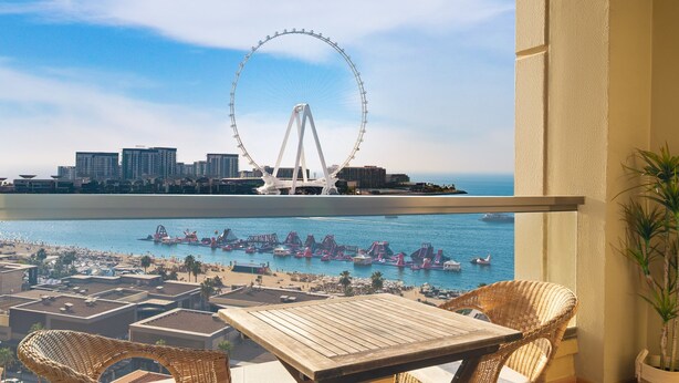 A balcony with wicker furniture overlooking a waterfront with a Ferris wheel and city buildings. - LUX  The Dubai Eye View JBR Studio (Dubai)