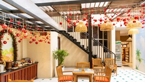 Un vestíbulo de hotel con una escalera, sillas de madera, una recepción y faroles rojos colgantes.