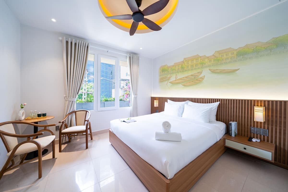 Camera d'albergo moderna con un letto grande, un comodino in legno, una scrivania con sedia e un'ampia finestra con tende.