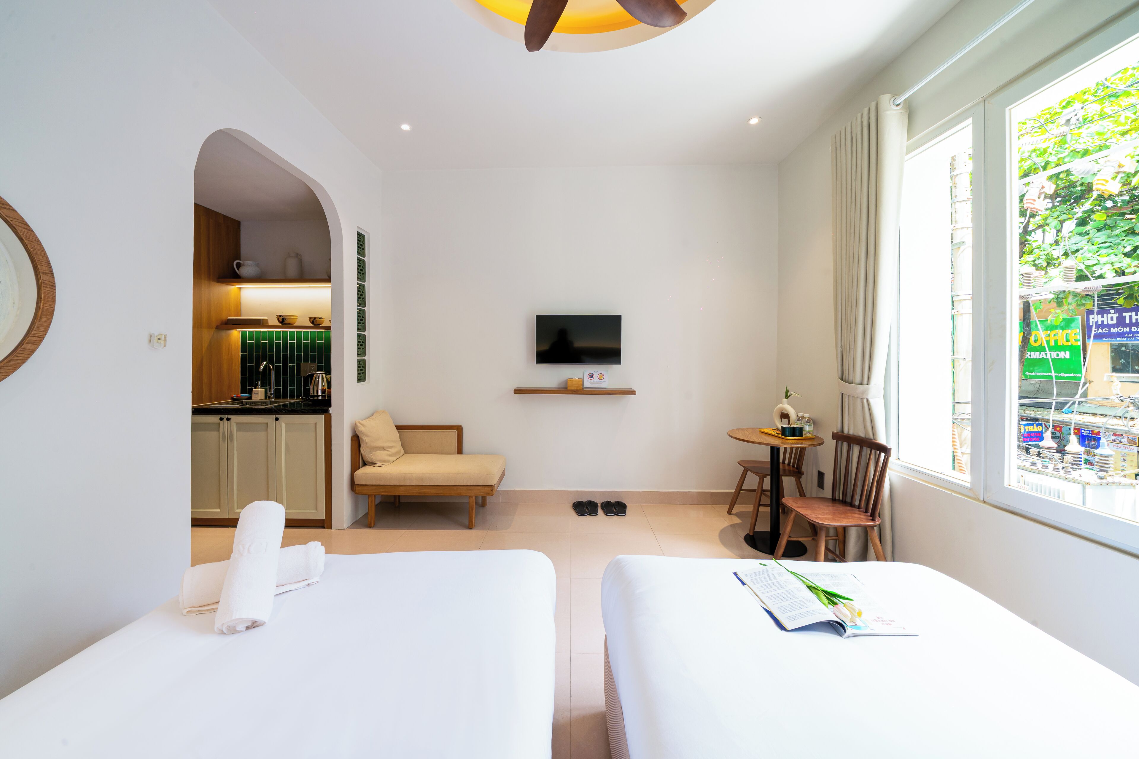 A hotel room with two beds, a TV, a small table, and a window with a view of the street.