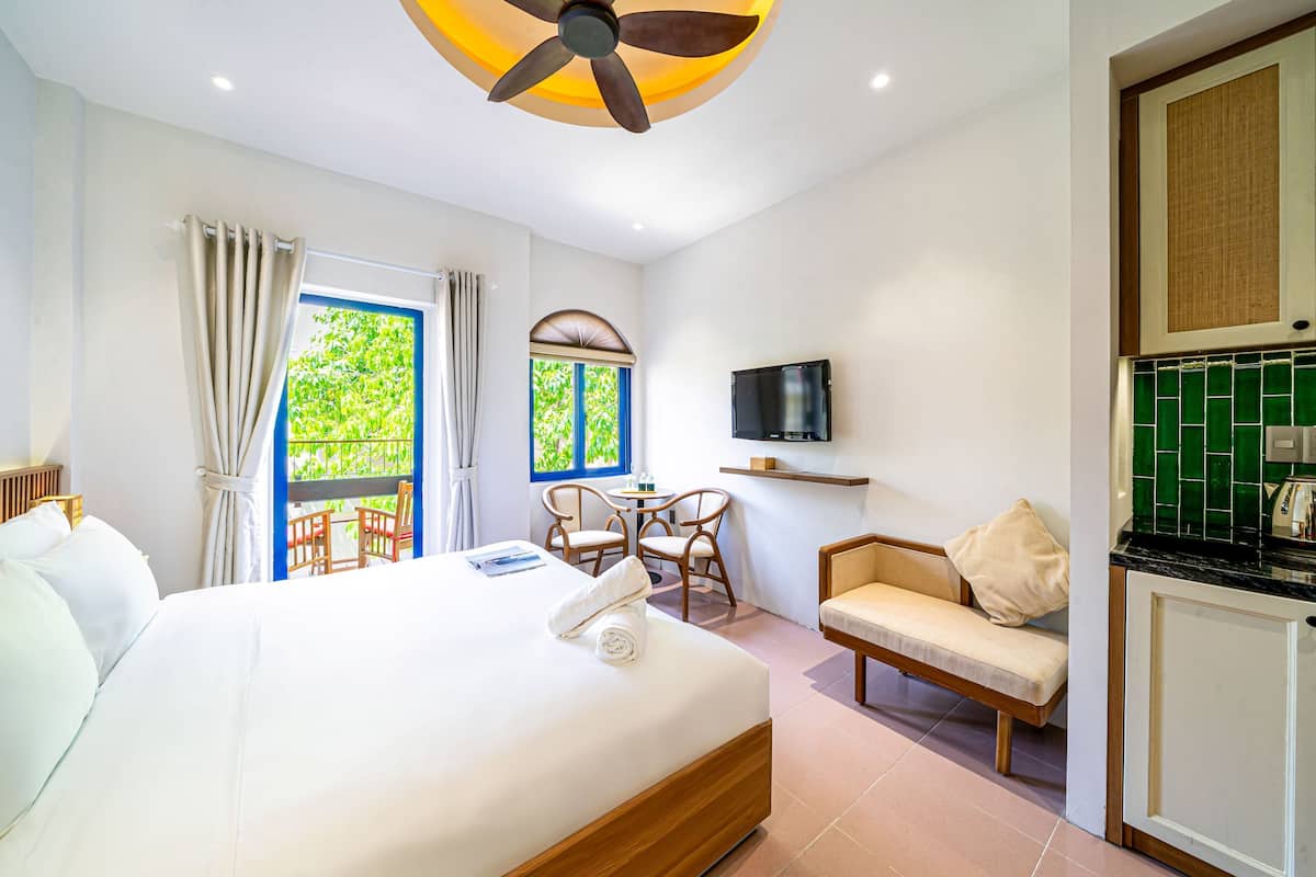 Una camera d'albergo con un letto, una televisione, un'area ristorazione e un balcone con vista sul verde.