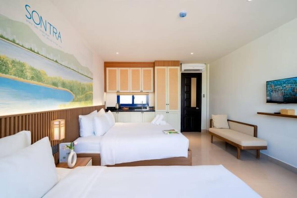 Una camera d'albergo con un letto, un divano, una televisione, un quadro e un angolo cottura.