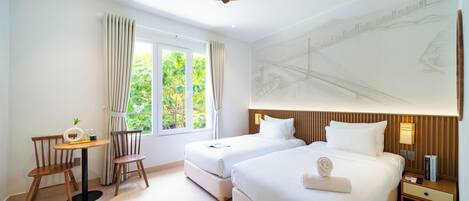 A hotel room with two beds, a desk with a chair, a ceiling fan, and a large window with curtains.