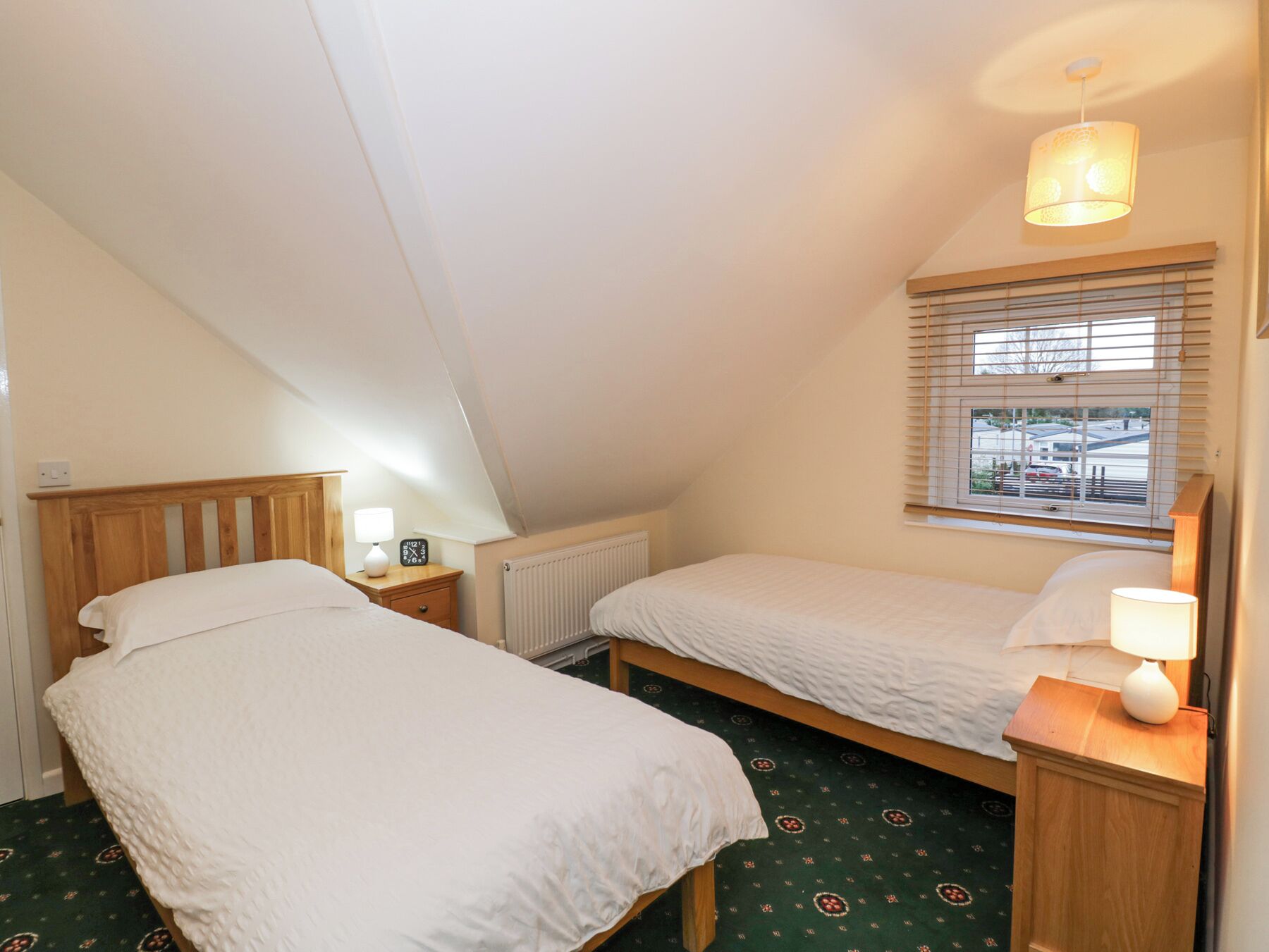 Een kleine, knusse slaapkamer met twee eenpersoonsbedden, een raam met zonwering, een radiator en een plafondlamp.