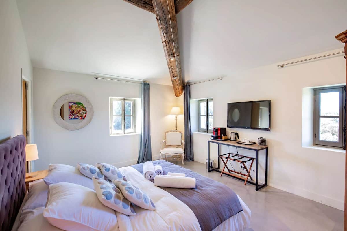 Een slaapkamer met een bed, bureau, stoel, televisie en raam.