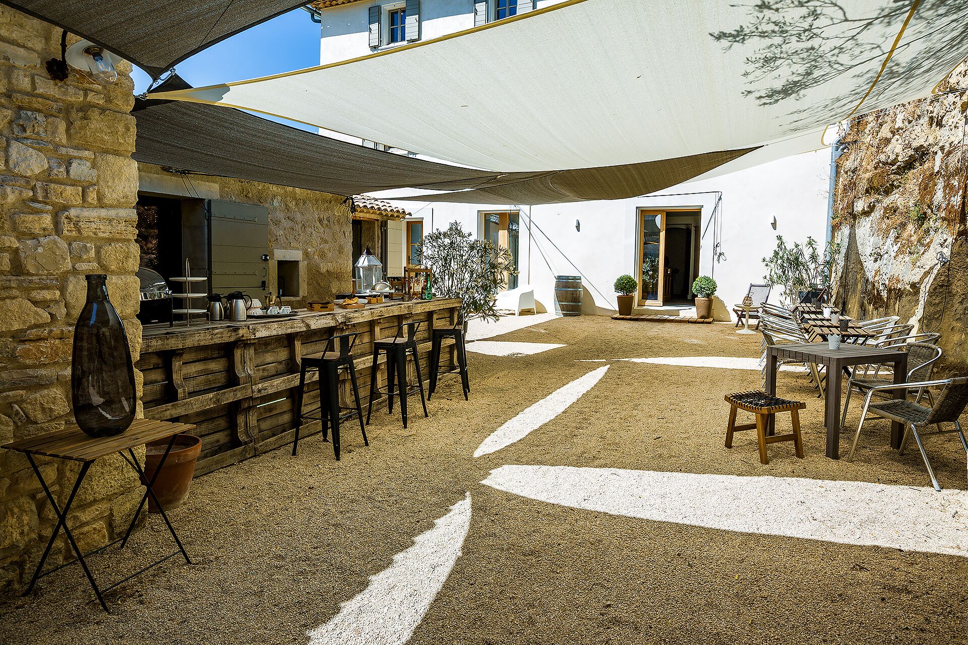 Un espace de restauration extérieur de style rustique, doté d’un bar, de murs en pierre et d’un coin salon ombragé.