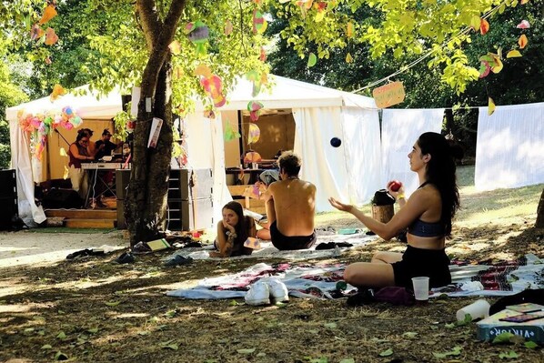 Un grupo de personas sentadas en el suelo bajo una tienda de campaña, con un árbol al frente.