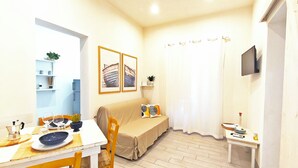 A compact living space with a dining area, a sofa, a small table, and a television mounted on the wall. - Summer House (Trapani)