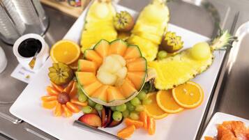 A fruit platter with various fruits and a small dish of sauce on a tray.