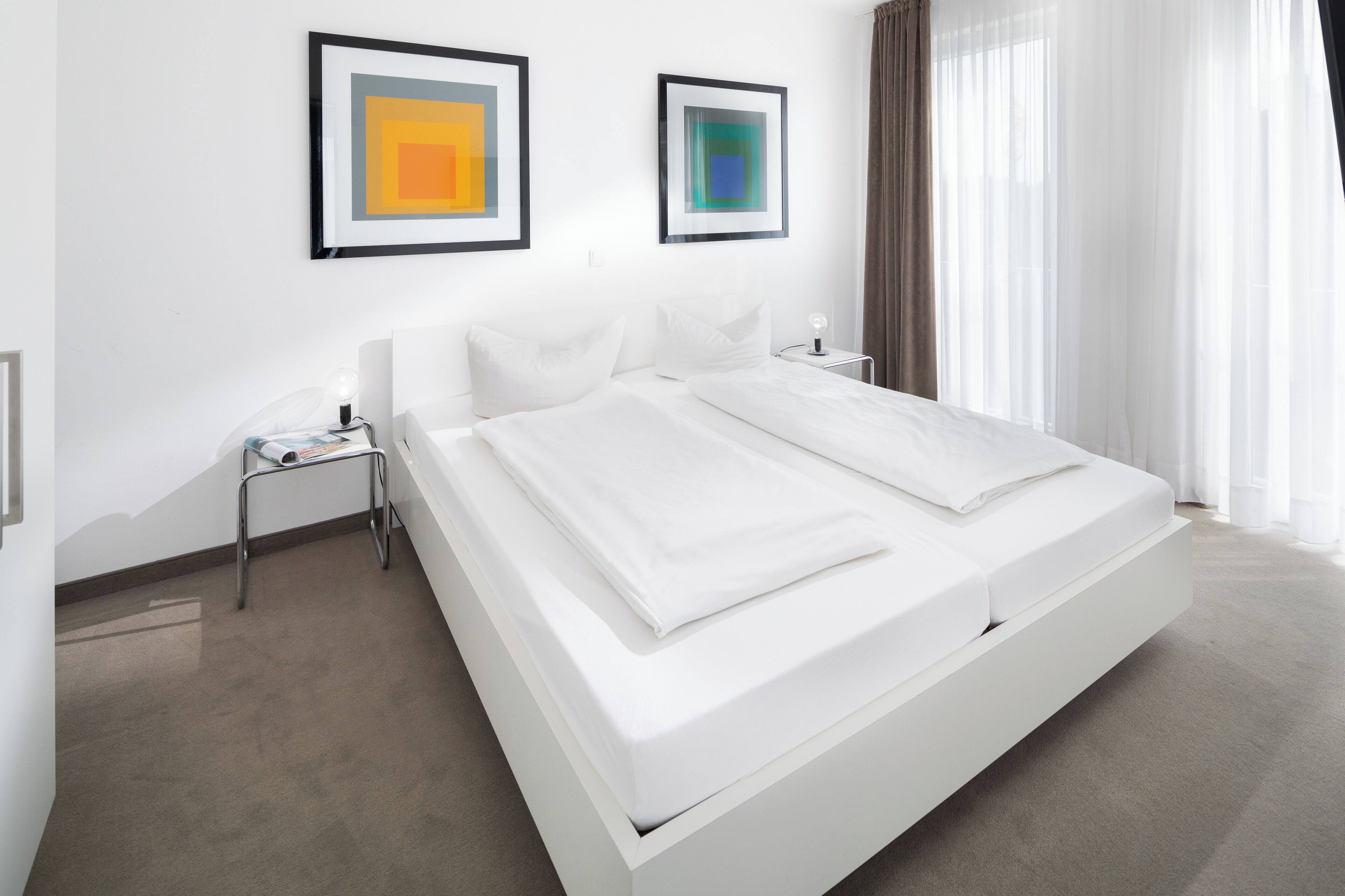 A modern hotel room with a large bed, a bedside table, and two framed artworks on the wall.