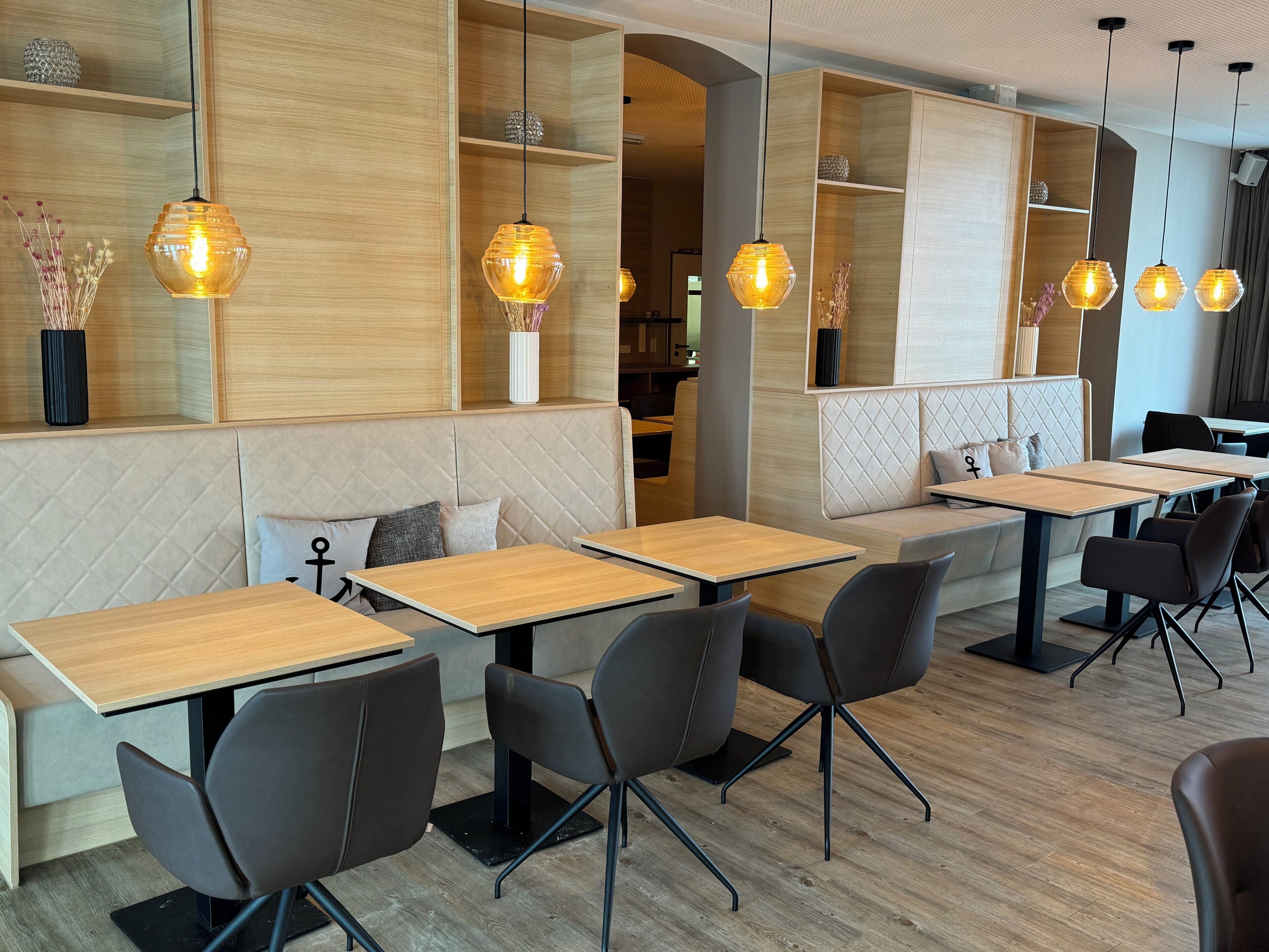 Un interior de restaurante moderno con mesas de madera, sillas negras e iluminación colgante.