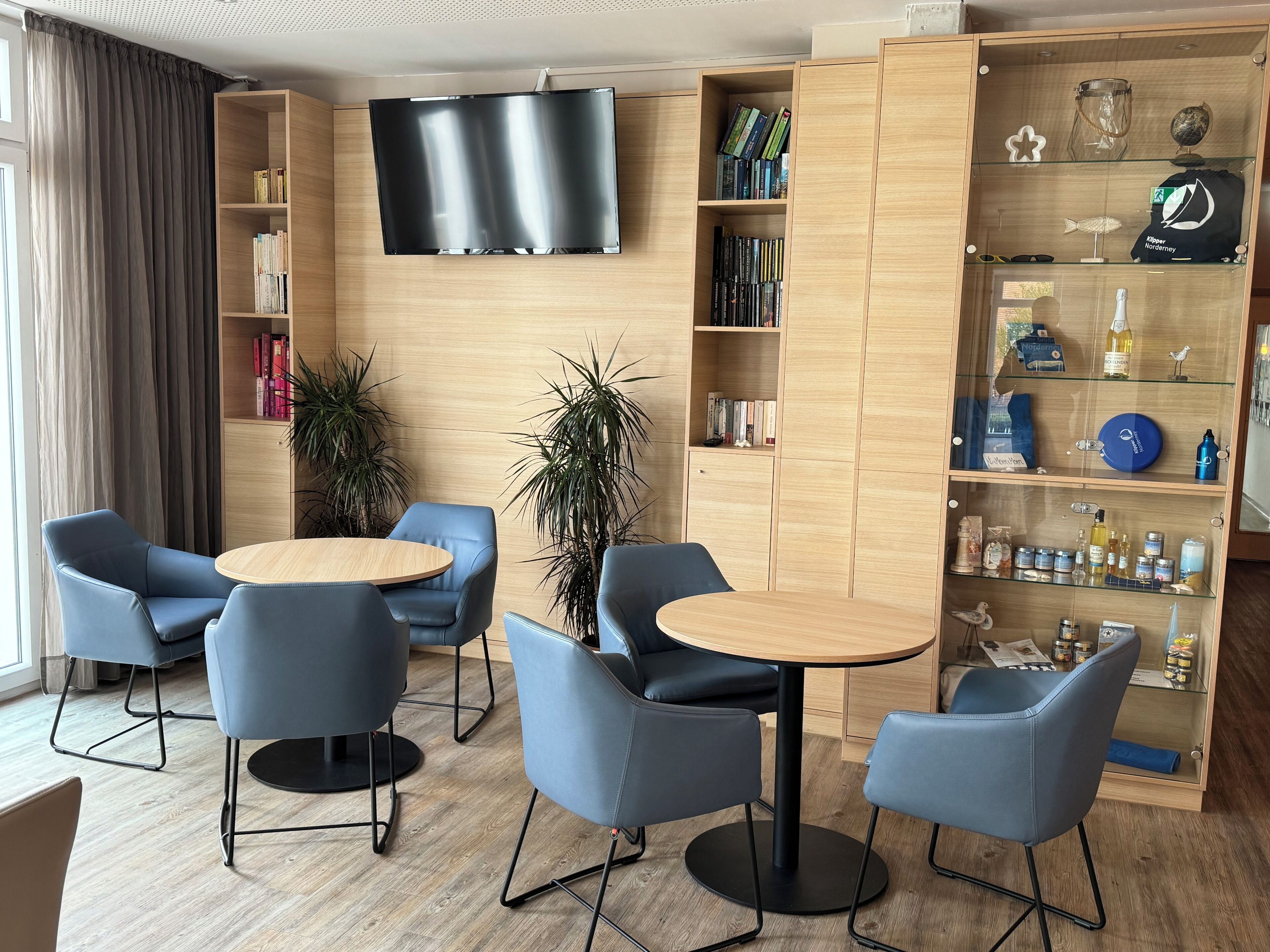 A modern hotel lobby with a flat-screen TV, a wooden bookshelf, and seating areas.