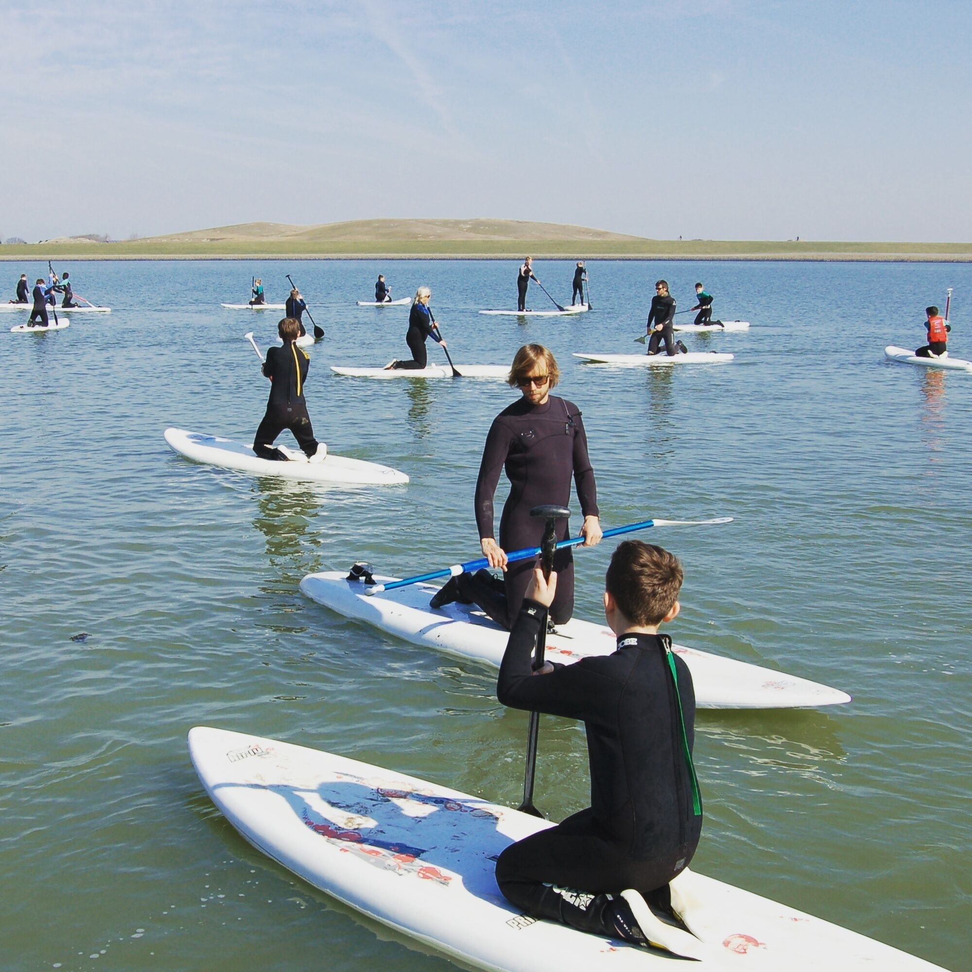 Un grupo de personas en tablas de remo sobre aguas tranquilas, probablemente un lago o el mar.