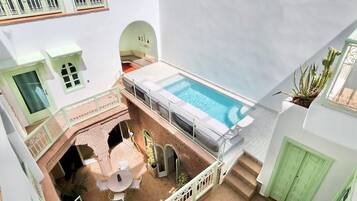 Un espace piscine aménagé sur le toit, avec une table et des chaises, entouré de murs blancs et agrémenté de touches de vert.