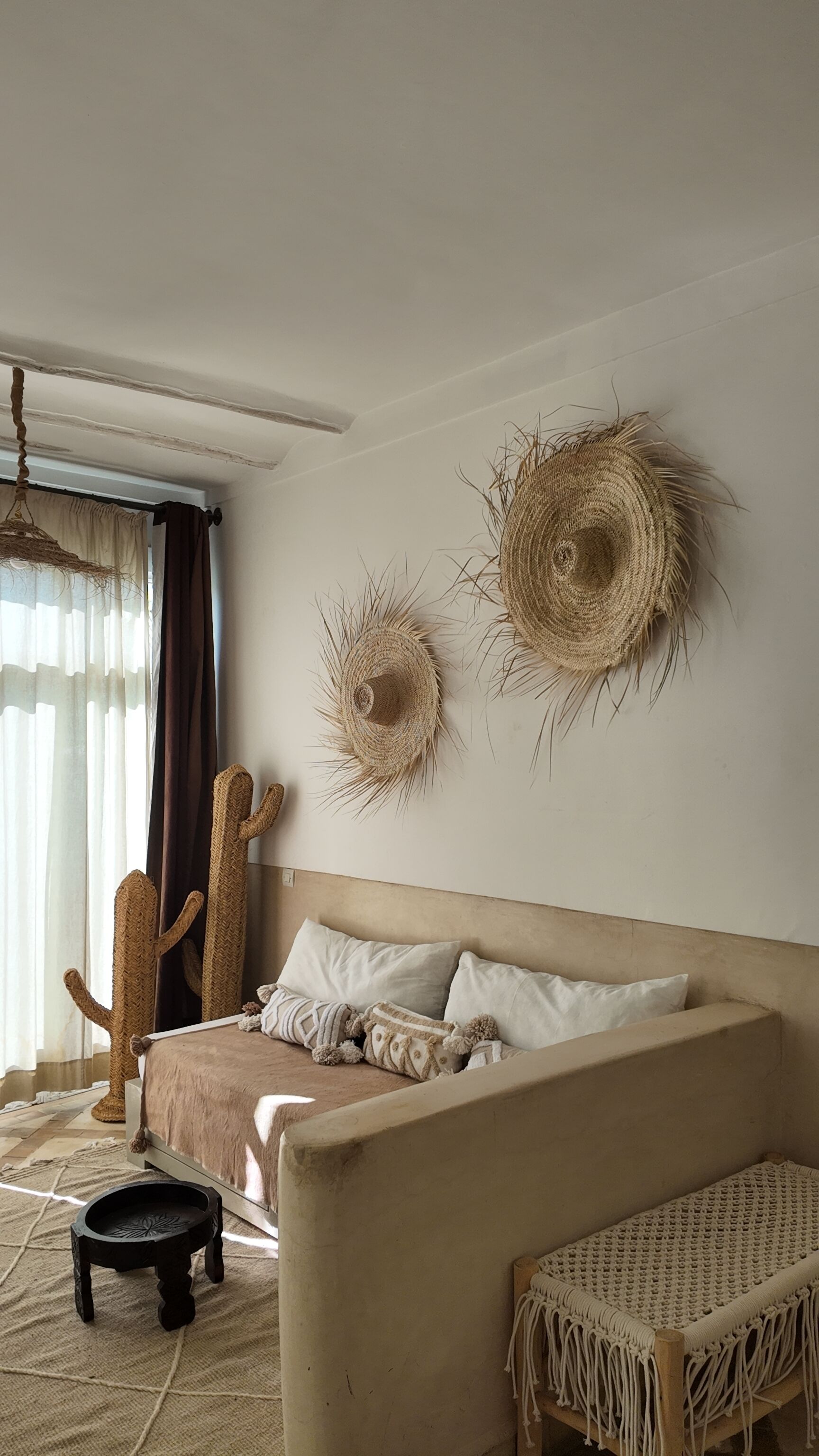 Ein Schlafzimmer mit einem Bett, einem Makramee-Sessel, einem kleinen Tisch und zwei Wandtextilien.