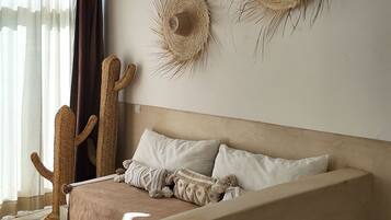 Ein Schlafzimmer mit einem Bett, einem Makramee-Sessel, einem kleinen Tisch und zwei Wandtextilien.